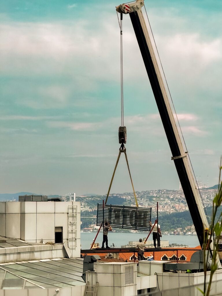 A crane lifting construction material above İstanbul skylines with workers on rooftops.